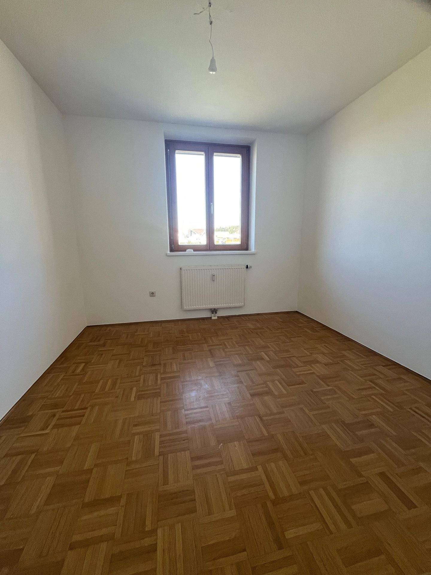 Geräumiges Zimmer mit Parkettboden, großem Fenster und viel natürlichem Licht, vielseitig nutzbar.