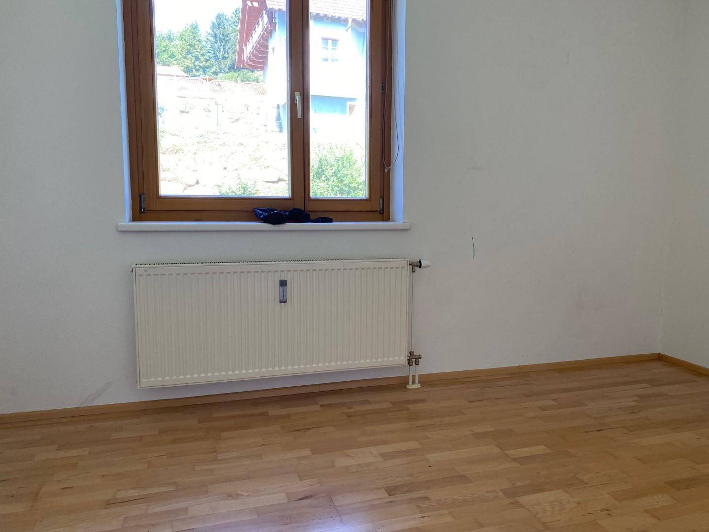 Schlafzimmer mit hellem Parkettboden, großem Fenster und Blick ins Grüne.