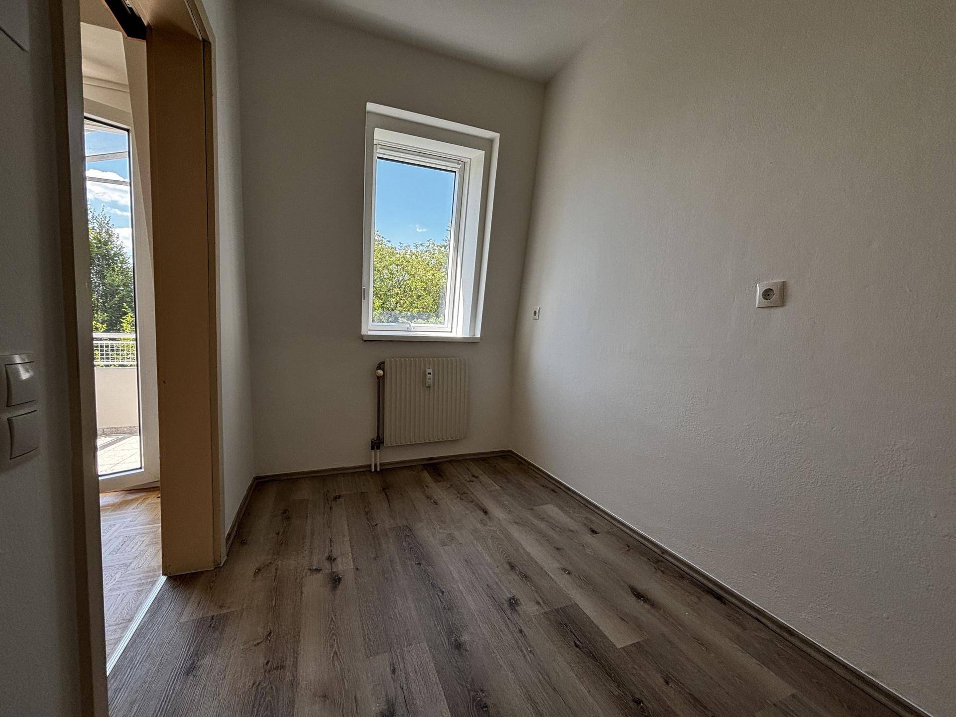 Helles Schlafzimmer mit Dachschräge, Fenster und Holzboden, bietet eine gemütliche Atmosphäre.