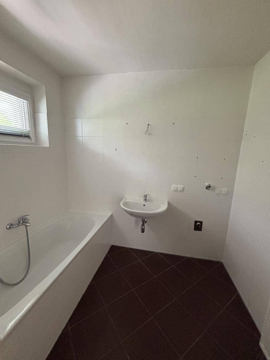 Helles Badezimmer mit Badewanne, Waschbecken und Fenster, ausgestattet mit Fliesenboden.