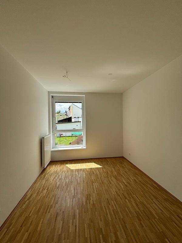 Sonniger Raum mit Parkettboden, Heizkörper und einem Fenster mit Blick ins Grüne.