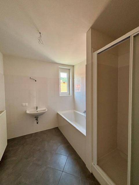 Modernes Badezimmer mit dunklen Fliesen, Badewanne, Duschkabine und einem Fenster für Tageslicht.