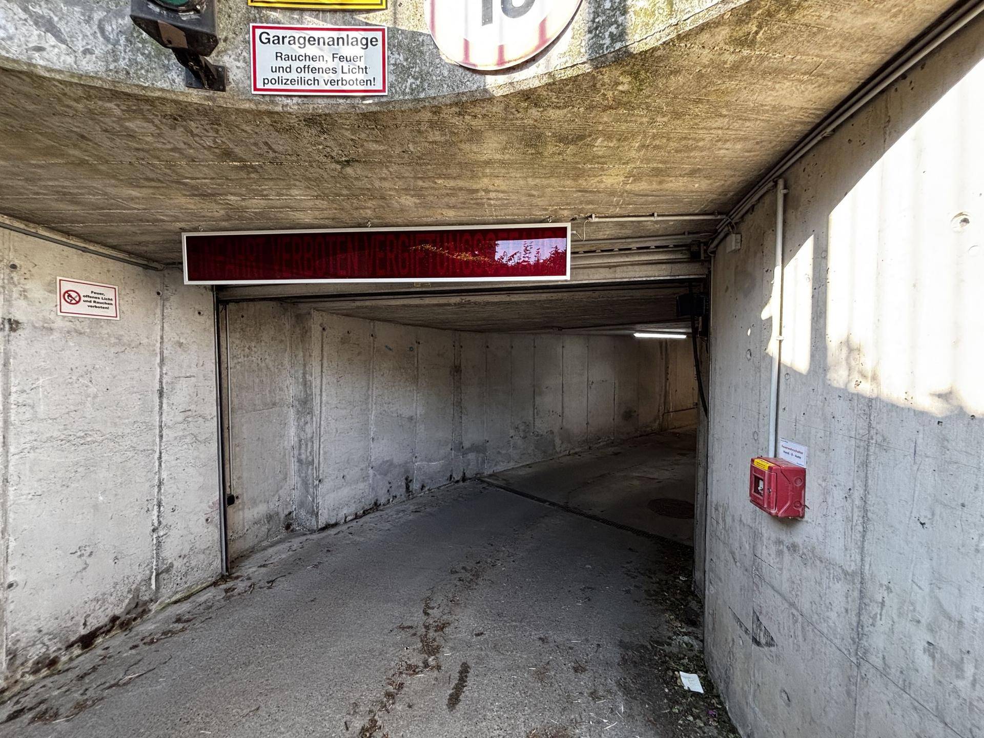 Einfahrt zu einer Tiefgarage mit Betontunnel und Hinweisschildern am Eingangsbereich.
