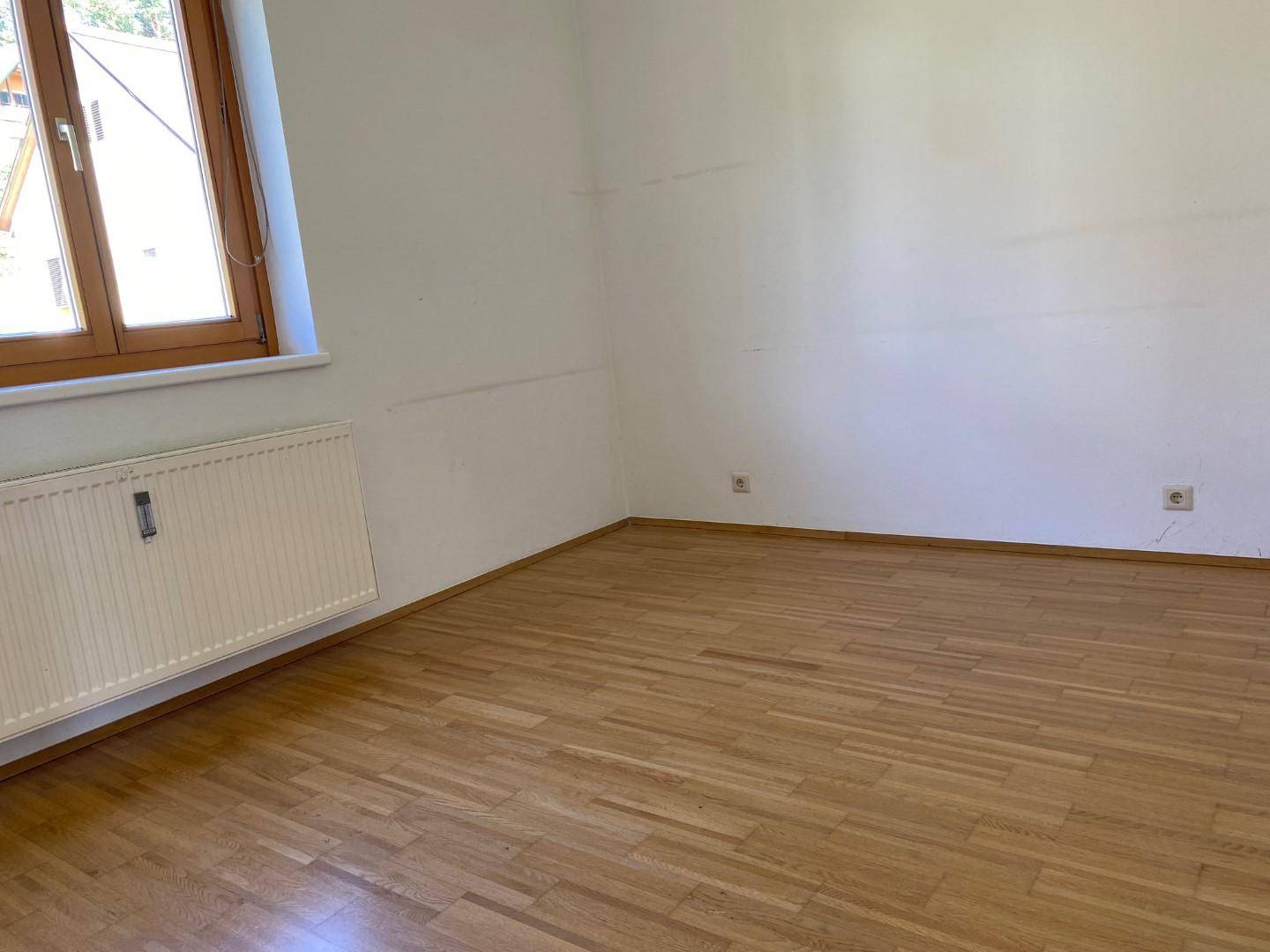 Leerer Raum mit Laminatboden und einem Fenster, das für natürliche Belichtung sorgt.