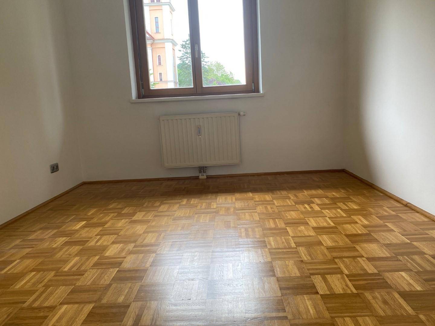 Leeres Zimmer mit Parkettboden, weiß gestrichenen Wänden und großem Fenster.