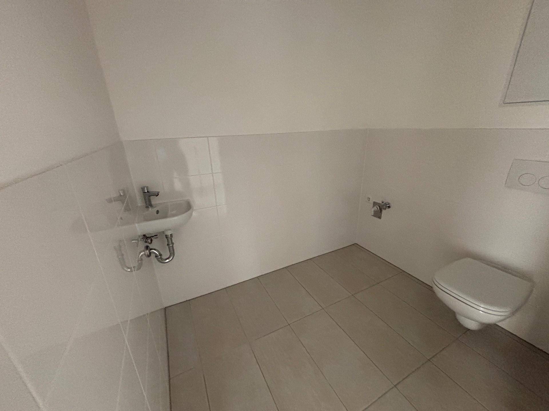 Modernes Gäste-WC mit weißen Fliesen, wandhängendem WC und kleinem Waschbecken.