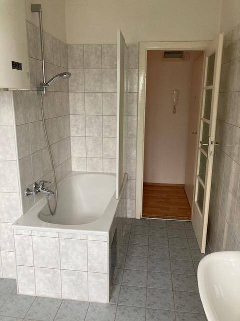 Badezimmer mit Badewanne, Duschvorrichtung und hellgrauen Wandfliesen.