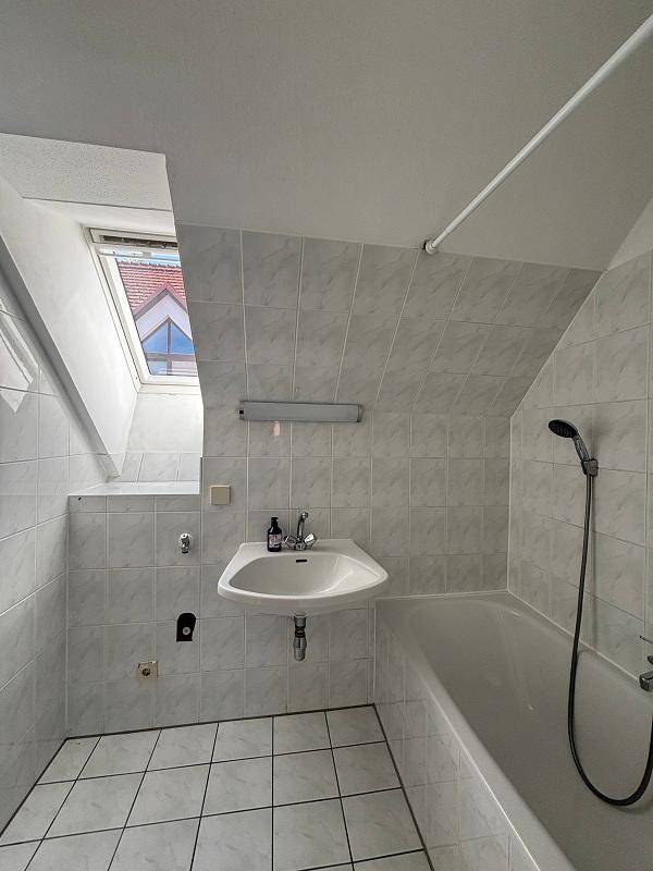Badezimmer mit weißen Fliesen, Badewanne, Waschbecken und Dachfenster, unter einer Dachschräge gelegen.