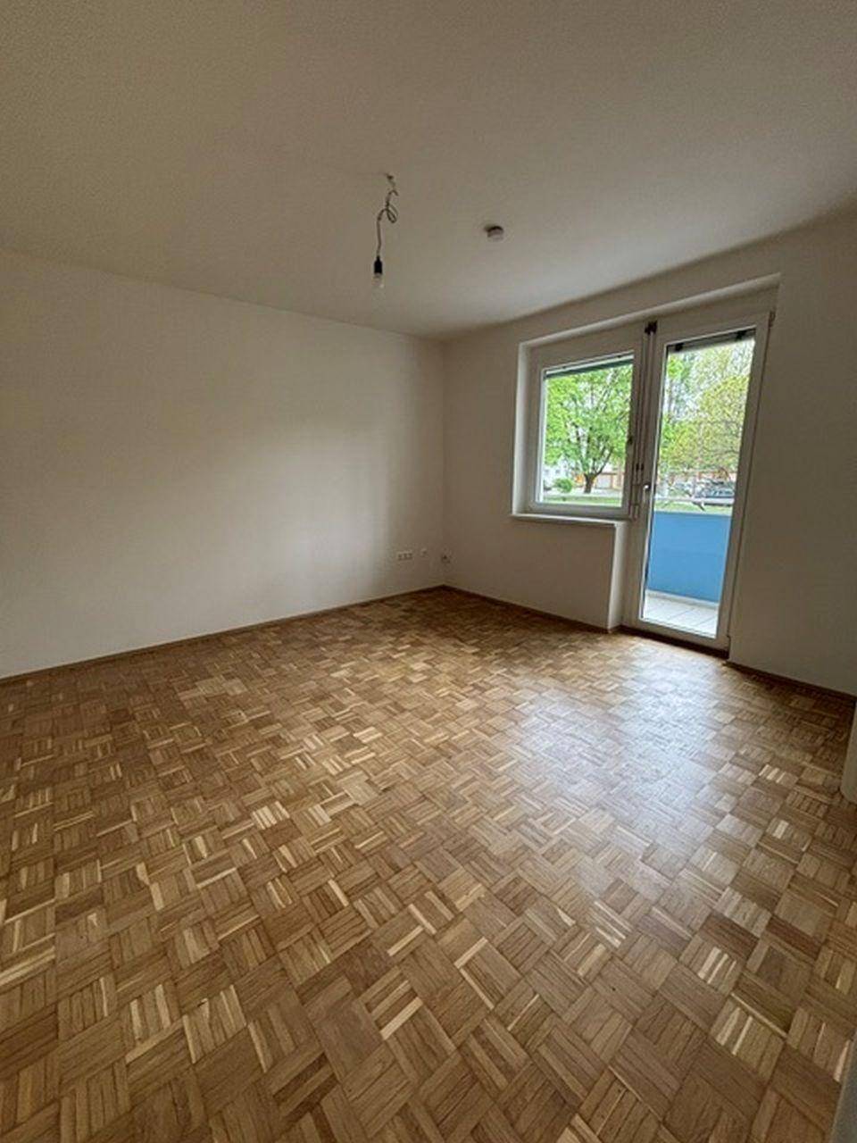 Geräumiges Wohnzimmer mit Parkettboden und Zugang zu einem Balkon, der viel Licht hereinlässt.
