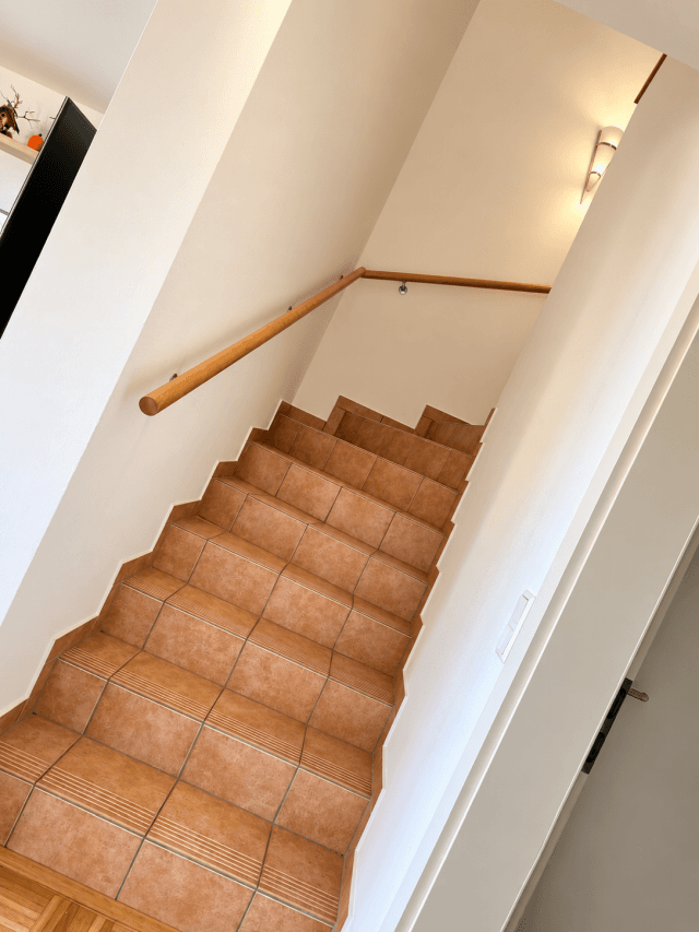 Heller Treppenaufgang mit Fliesenboden und Holzgeländer, gut beleuchtet.