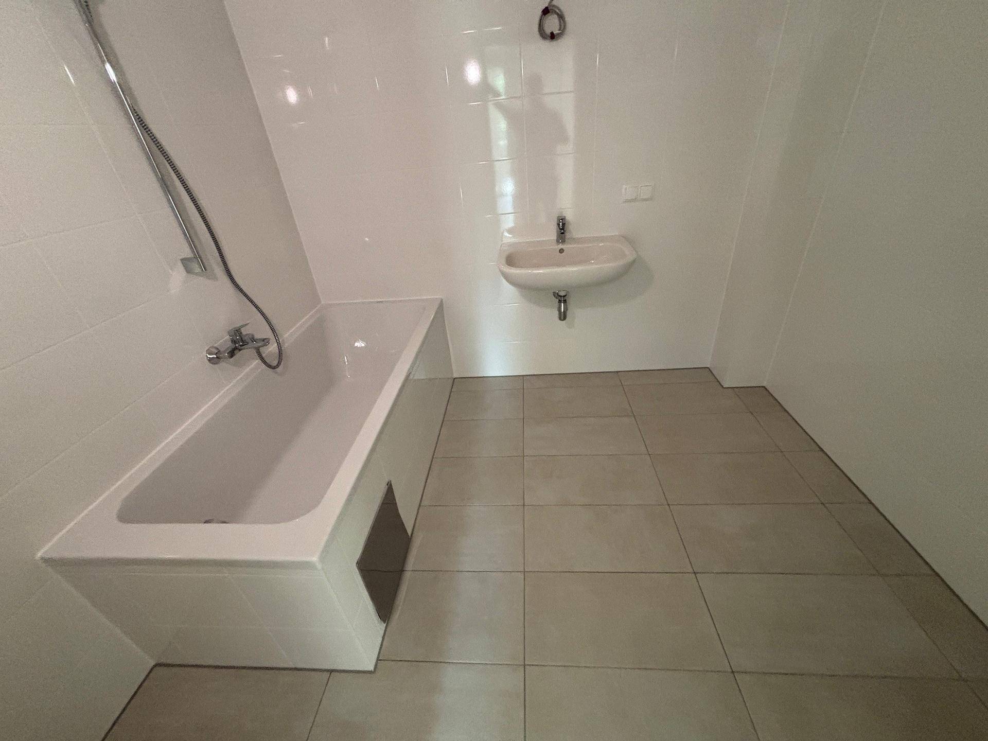 Helles Badezimmer mit Badewanne, integrierter Dusche und kleinem Waschbecken.
