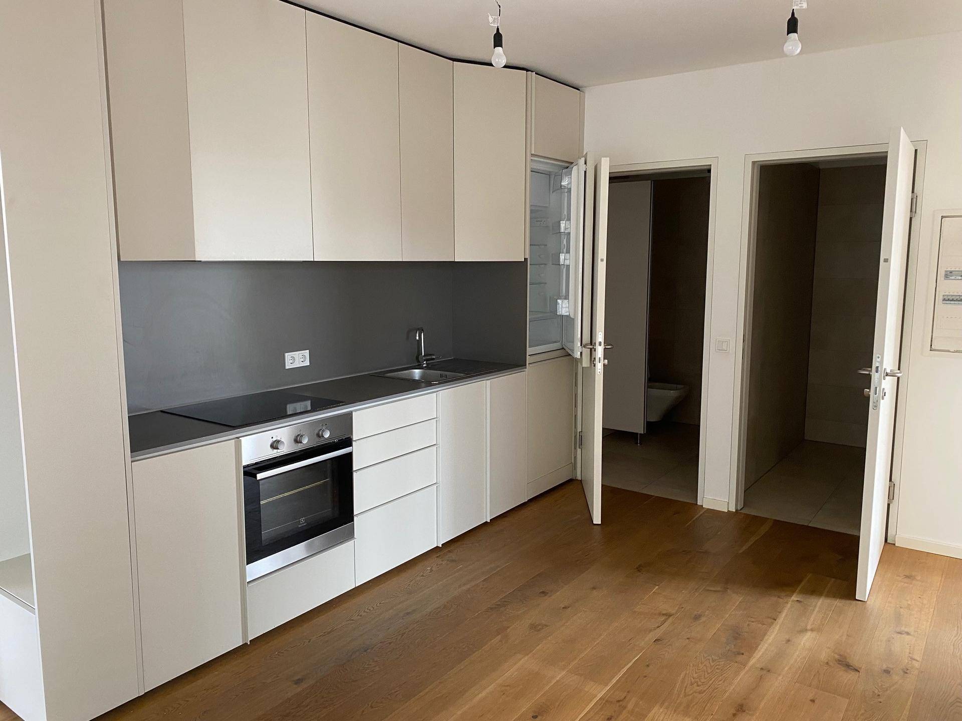 Moderne Einbauküche in hellem Beige mit integrierten Geräten und Holzboden, angrenzend an weitere Räume.