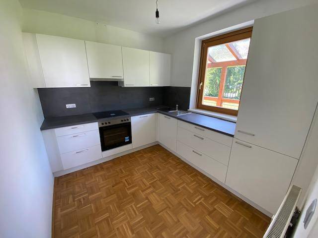 Moderne Küche mit weißen Schränken, dunkler Arbeitsplatte, Herd und Parkettboden.
