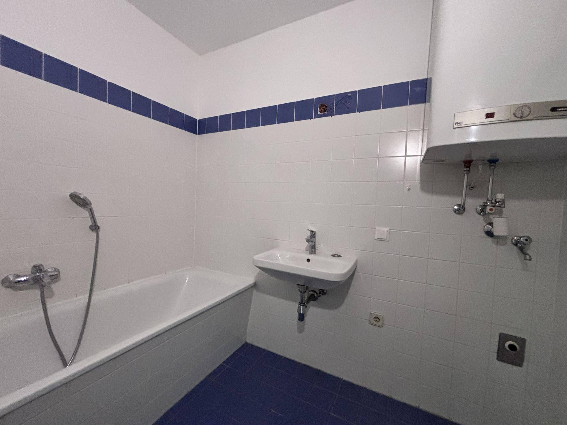 Badezimmer mit Badewanne, Waschbecken und blauen Fliesenstreifen an den Wänden.