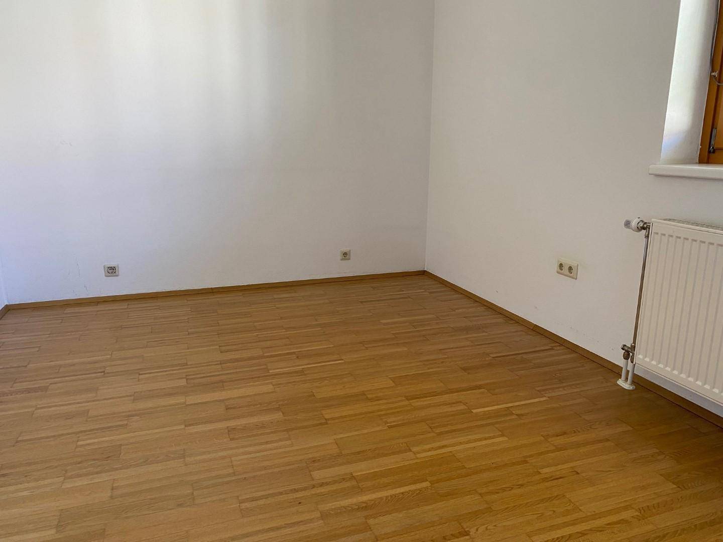 Geräumiger Raum mit Laminatboden und einem Fenster, ideal als Schlaf- oder Wohnzimmer.