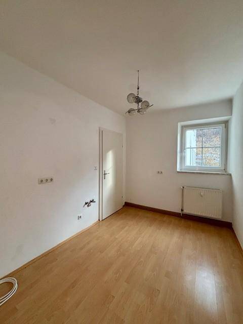 Helles Zimmer mit Laminatboden, weiß gestrichenen Wänden und einem Fenster.