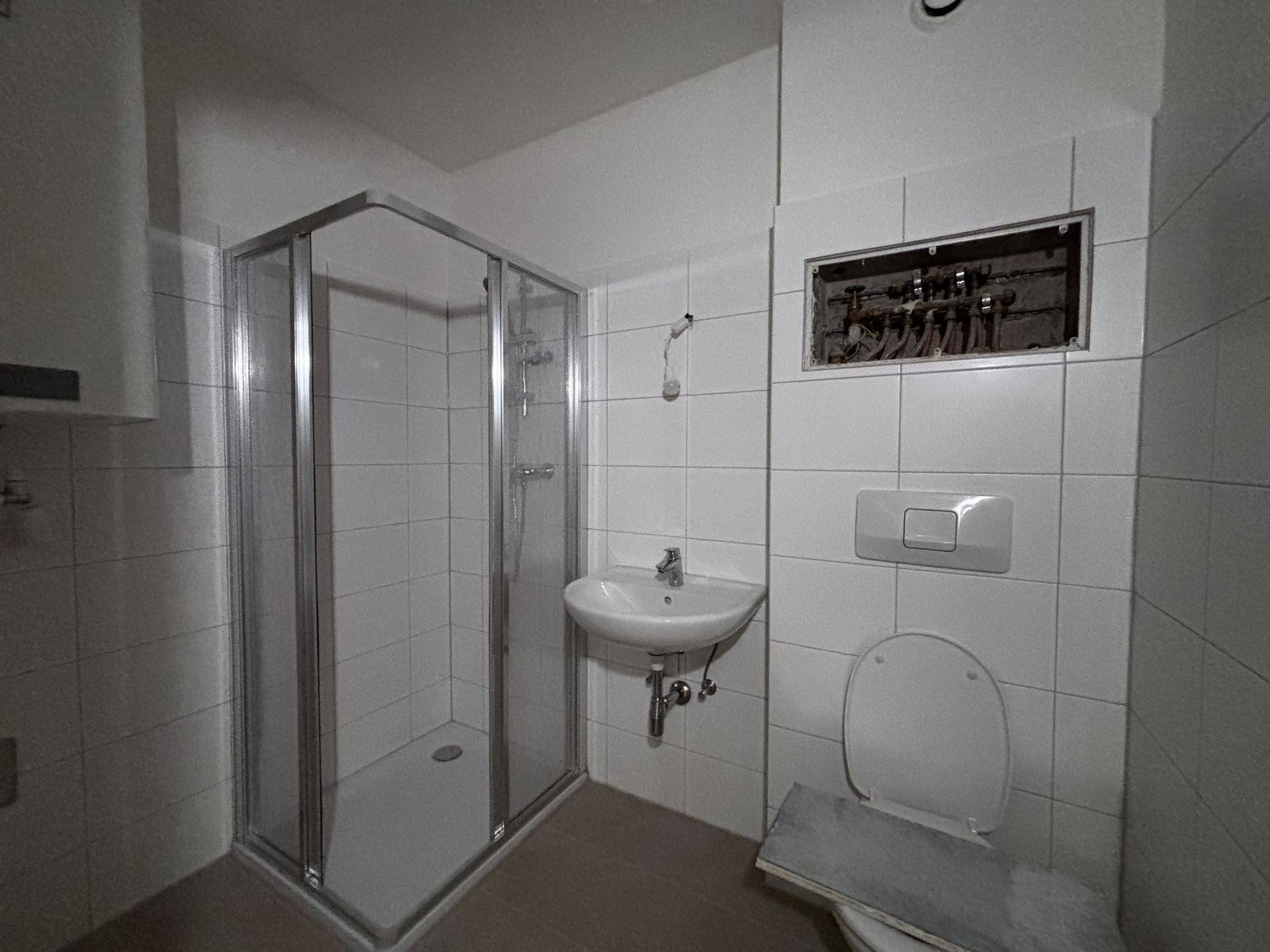 Badezimmer mit Duschkabine, Waschbecken und wandhängender Toilette in hellen Fliesen.