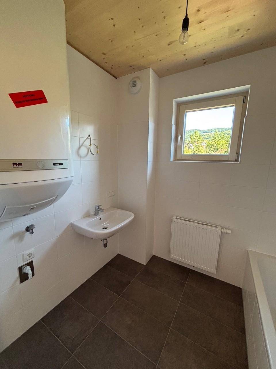 Badezimmer mit Waschbecken, Warmwasserbereiter, Fenster und Blick ins Grüne.