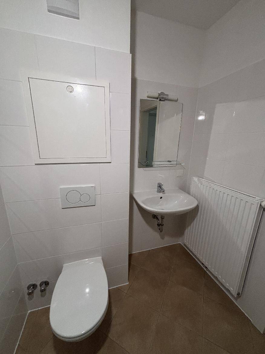 Funktionales Badezimmer mit Waschbecken, WC, Heizkörper und weißen Wandfliesen.
