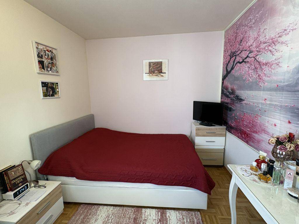 Gemütliches Schlafzimmer mit roter Bettdecke, Parkettboden und dekorativer Wandtapete.