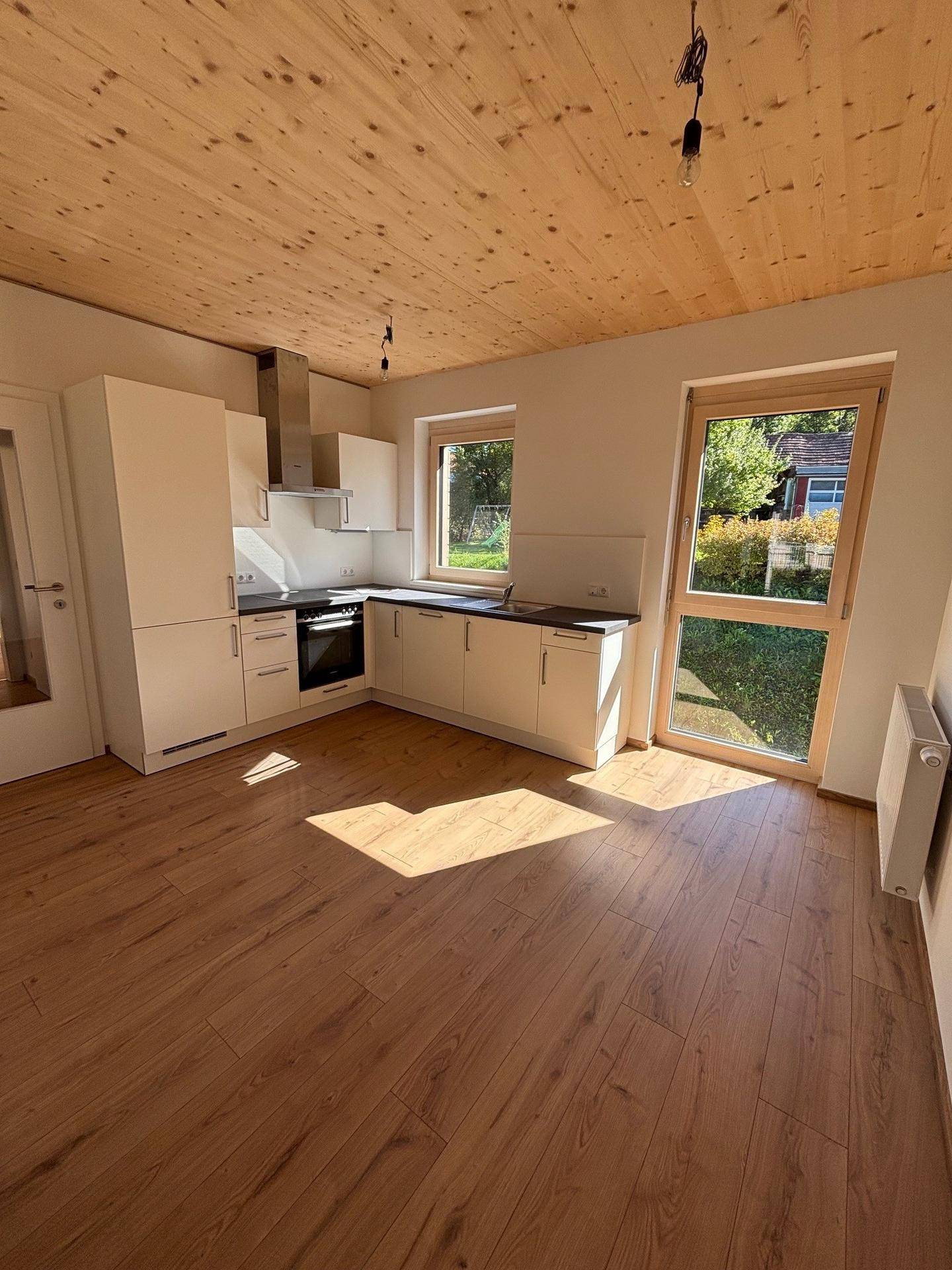 Moderne Küche mit weißen Schränken, Holzboden und Holzdecke, ausgestattet mit grundlegenden Geräten.