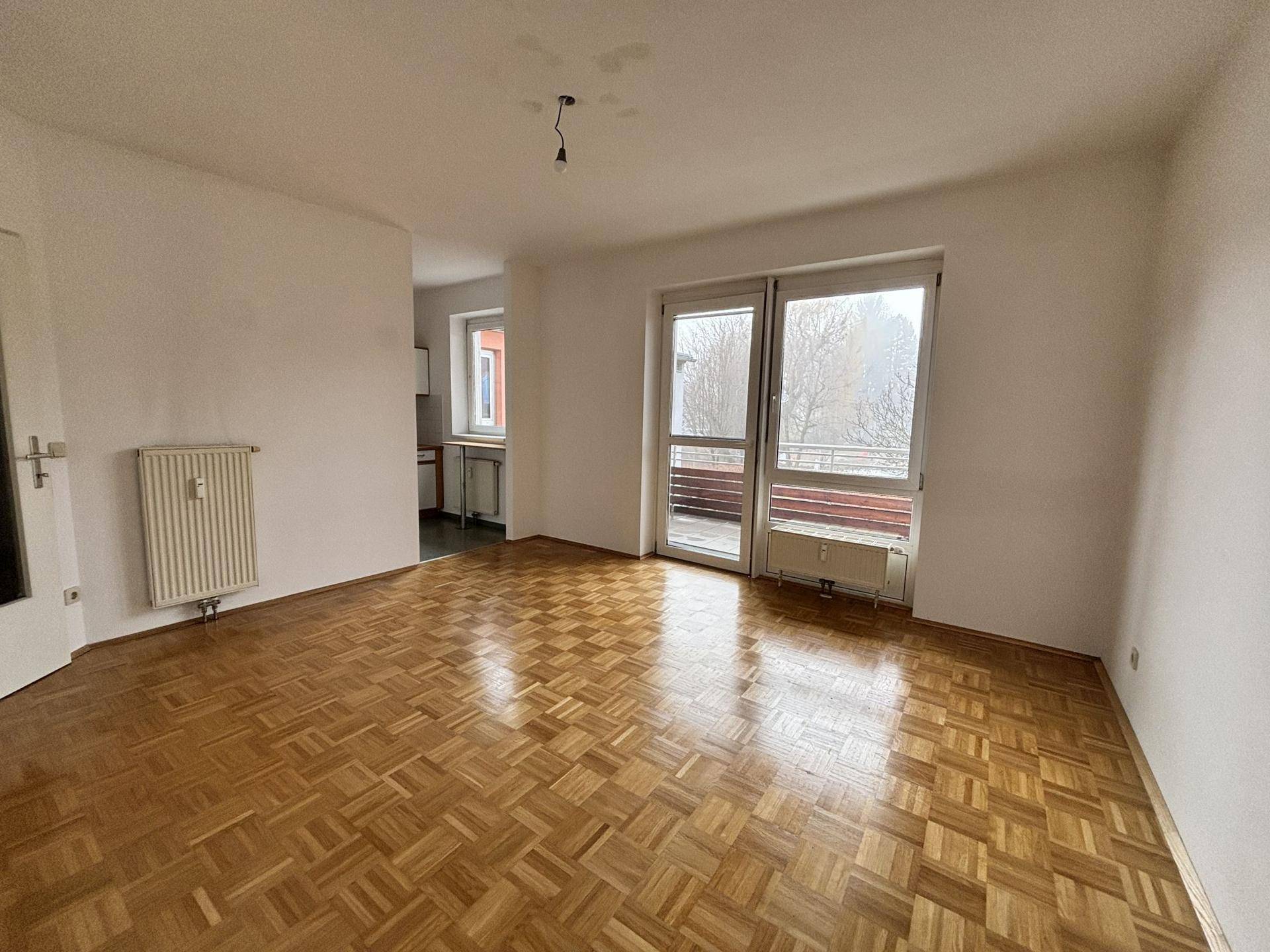 Geräumiges Wohnzimmer mit Parkettboden, Heizkörper und Zugang zum Balkon.
