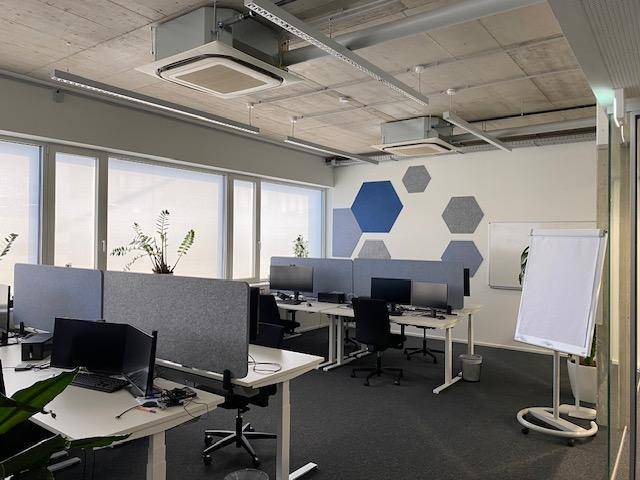 Moderner Großraumbüro mit ergonomischen Arbeitsplätzen, großen Fenstern und akustischen Wandpaneelen.