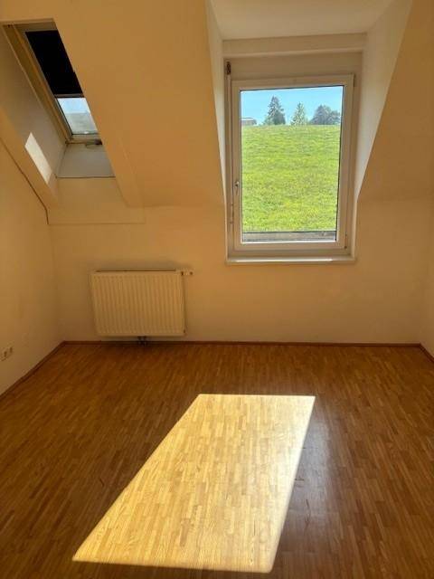 Helles Zimmer im Dachgeschoss mit Parkettboden, Dachfenster und Blick ins Grüne.