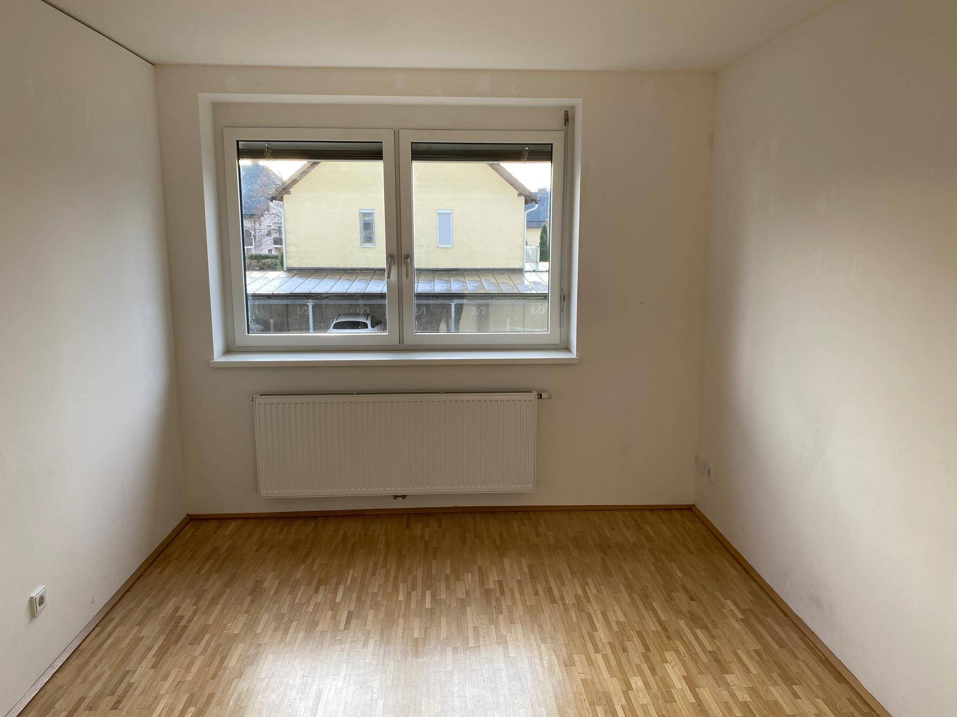 Helles Schlafzimmer mit Holzboden, großem Fenster und Heizkörper.