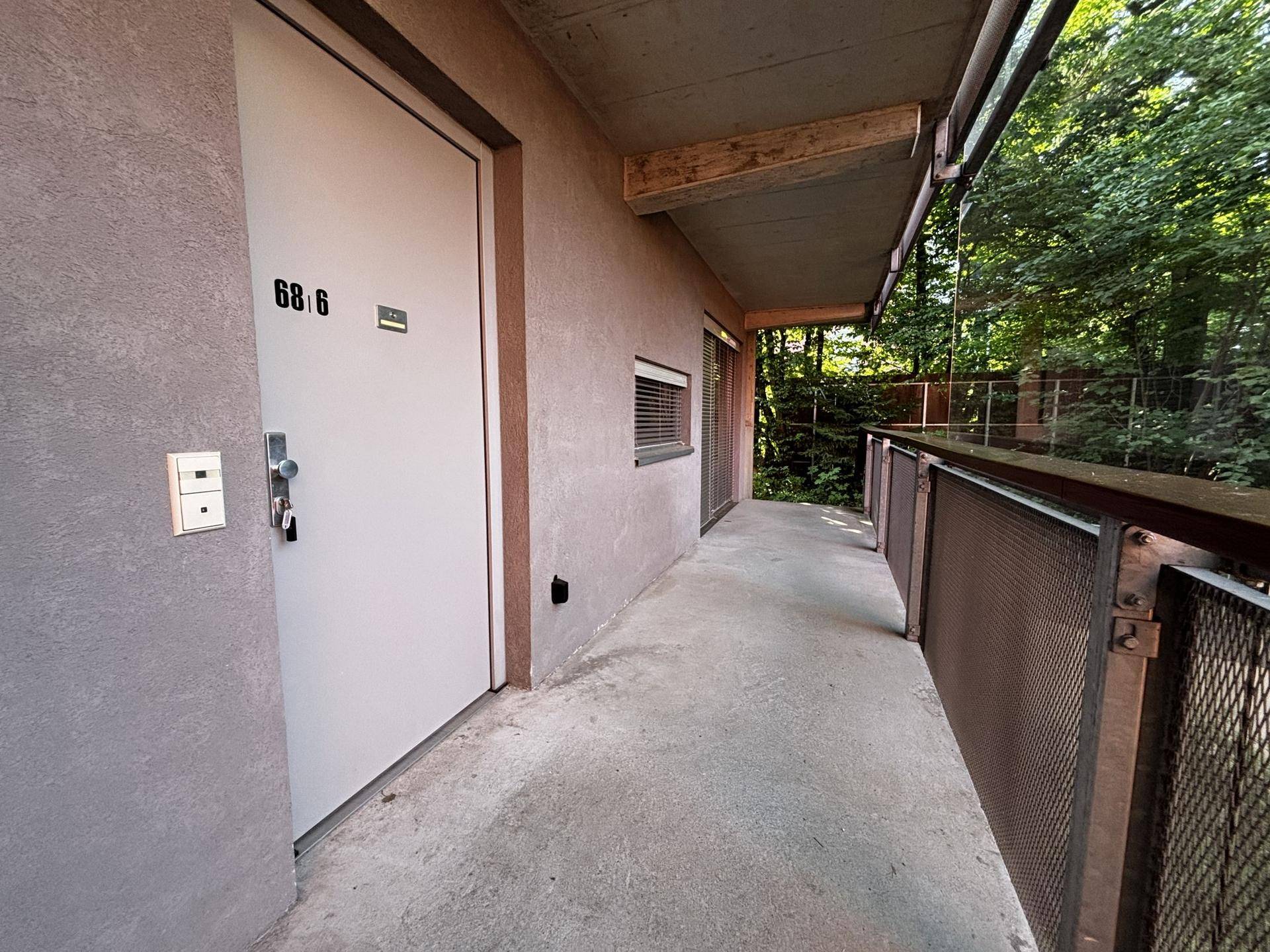 Zugang zur Wohnung 68/6 über einen langen Balkon, umgeben von üppigem Grün.