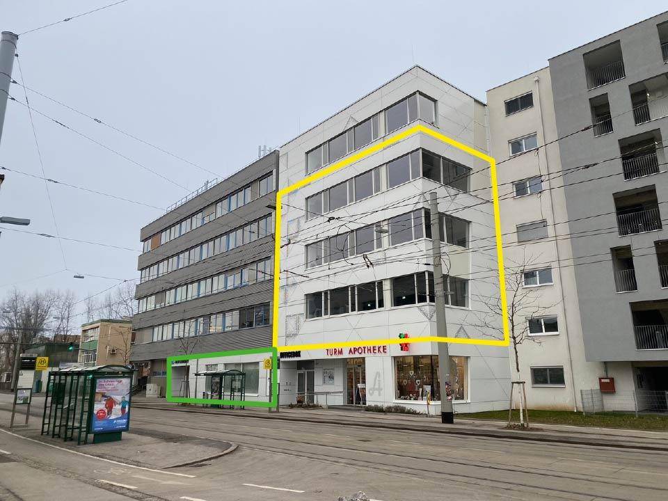 Modernes Gebäude mit Geschäftsflächen im Erdgeschoss, großen Fenstern und Balkonen an einer städtischen Straße.