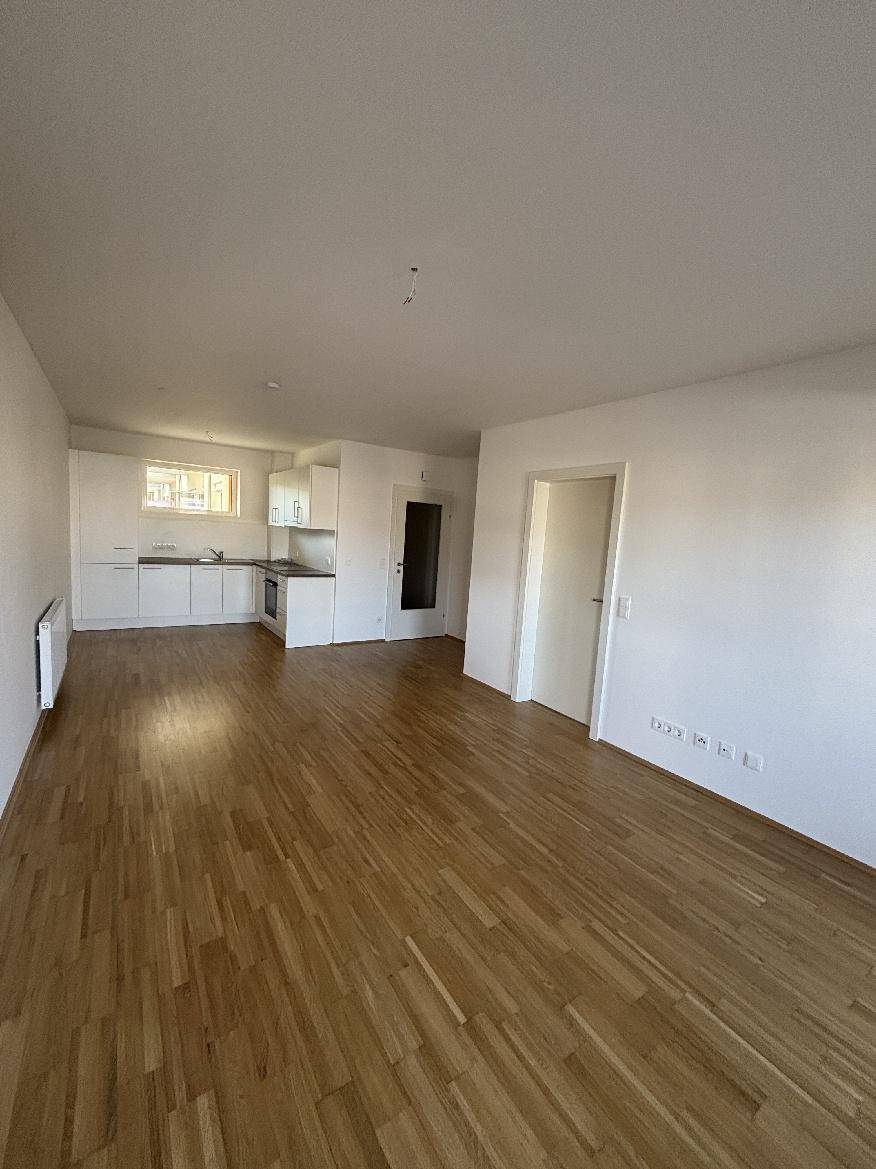 Heller offener Wohnbereich mit integrierter Küche und hochwertigem Holzparkettboden.