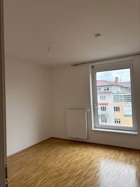 Leeres Schlafzimmer mit Parkettboden, weiß gestrichenen Wänden und Blick auf Nachbargebäude.