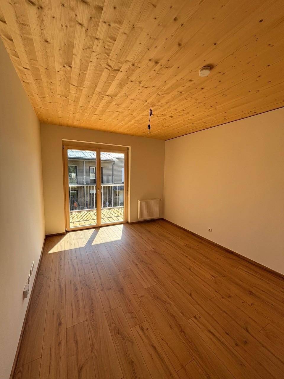 Helles Zimmer mit Holzboden und Holzdecke, Zugang zu einem Balkon und viel Tageslicht.