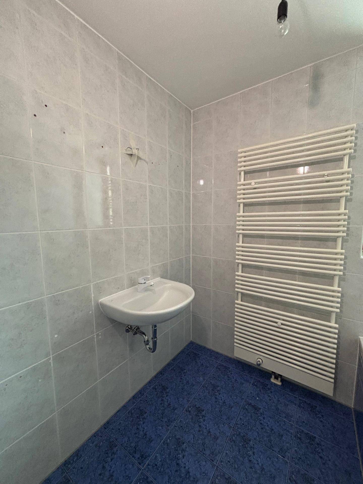 Badezimmer mit Waschbecken, Fliesenwänden und einem praktischen beheizten Handtuchhalter.