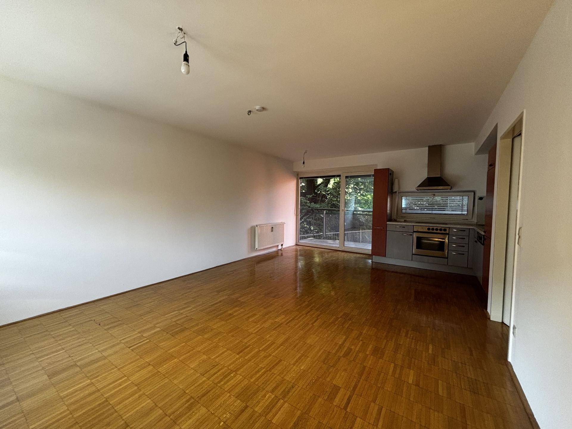 Offener Wohnbereich mit Parkettboden, Zugang zum Balkon und integrierter Küchenzeile.