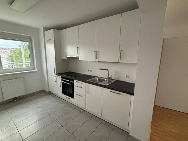 Moderne Einbauküche mit weißen Schränken, dunkler Arbeitsplatte und Fenster für natürliches Licht.
