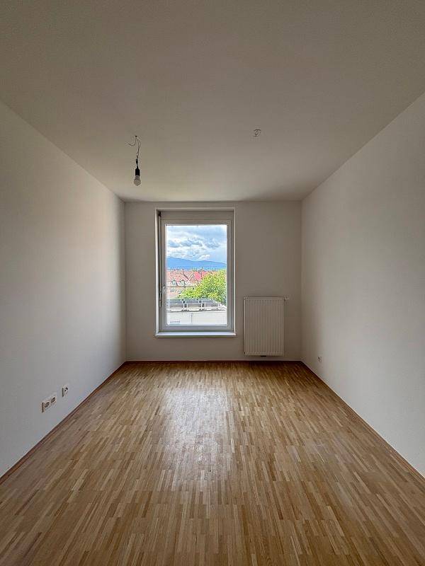 Geräumiges Zimmer mit Parkettboden und Fensterblick auf die Stadt und Berge.