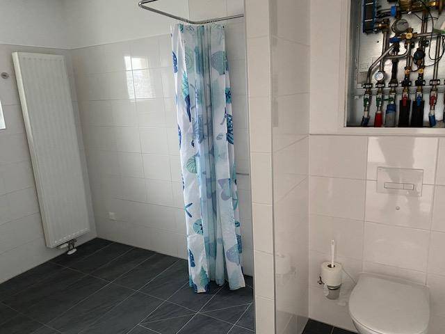 Modernes Badezimmer mit Dusche, WC, Heizkörper und sichtbaren Installationen.
