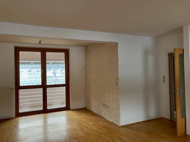 Leeres Zimmer mit Holzboden, großer Fenstertür und dekorativer Steinwand.