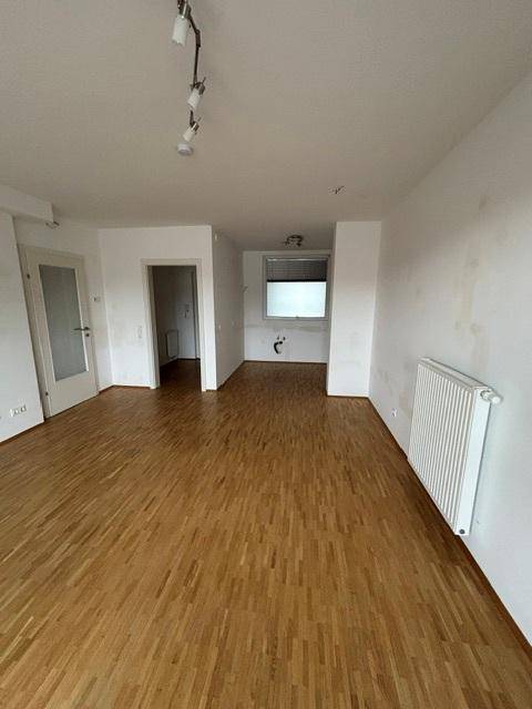 Offener Wohnbereich mit Parkettboden und Blick auf den zukünftigen Küchenbereich, ideal für modernes Wohnen.
