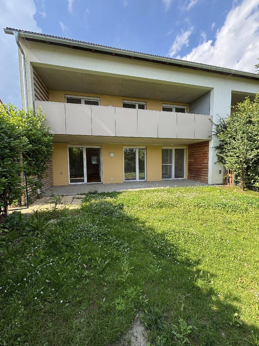 Rückseite des Gebäudes mit Garten, Terrasse und Balkonen unter strahlend blauem Himmel.