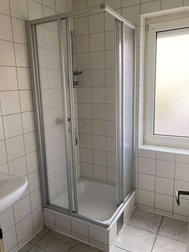 Helles Badezimmer mit Duschkabine, weißen Fliesen und Fenster.