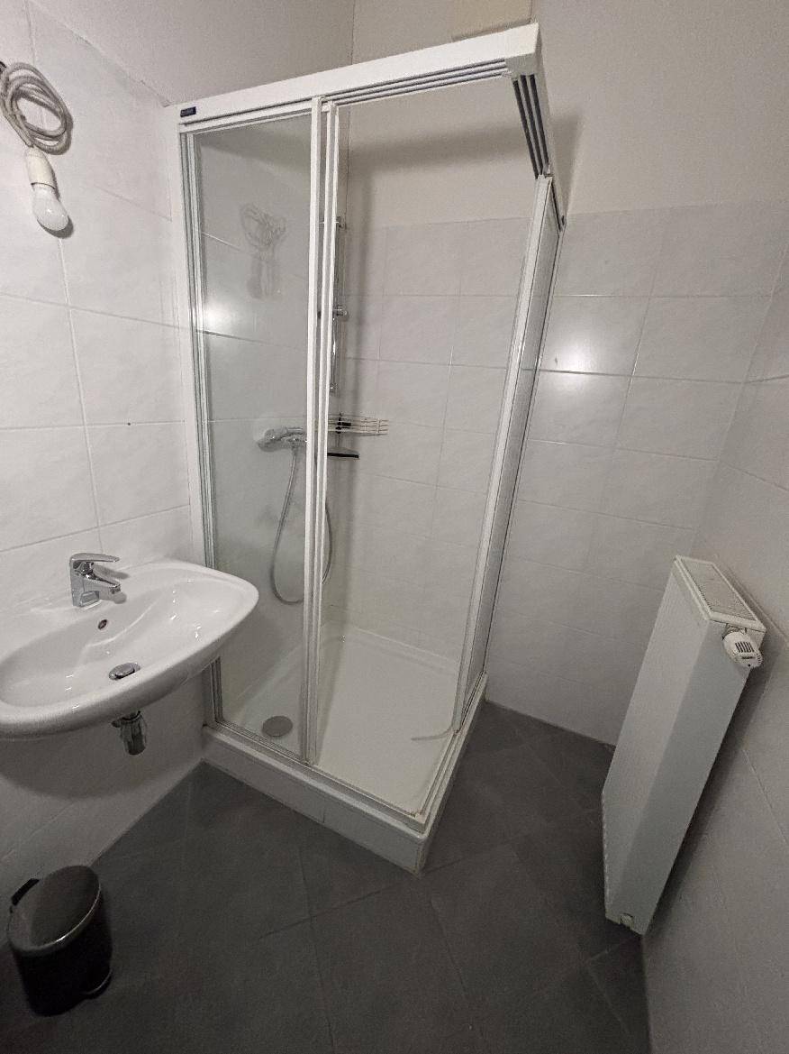 Badezimmer mit Duschkabine, Waschbecken und weißen Wandfliesen.