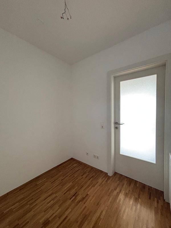 Leerer Raum mit hellem Parkettboden und einer Tür mit Milchglas, bereit zur individuellen Gestaltung.