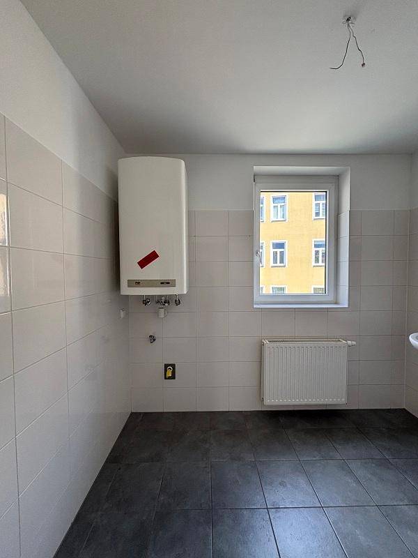 Raum mit Warmwasserbereiter, Heizkörper und Fenster, ideal als Hauswirtschaftsraum oder Abstellraum.