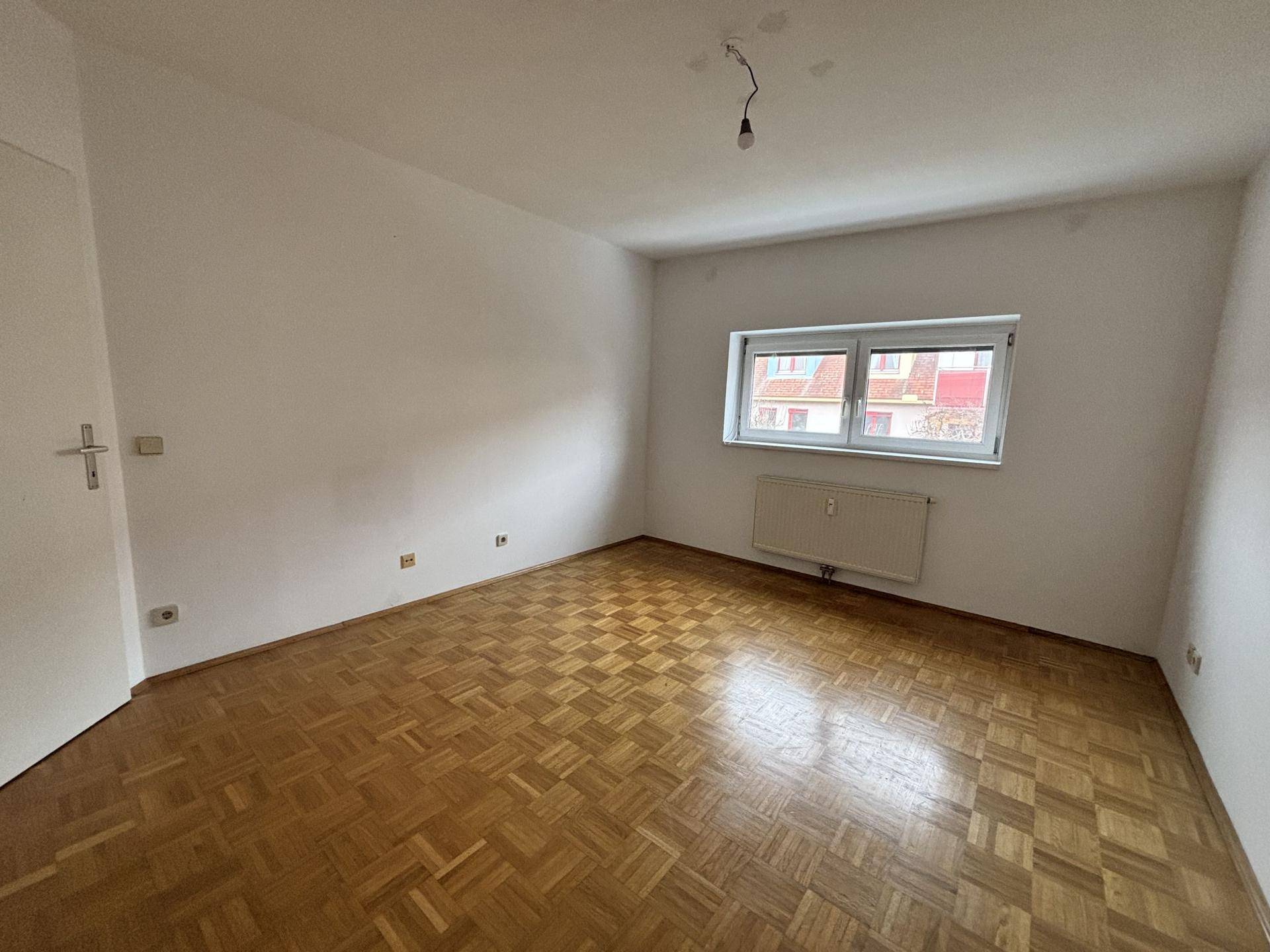 Schlafzimmer mit Parkettboden, Fenster und Heizkörper, bereit zur individuellen Gestaltung.