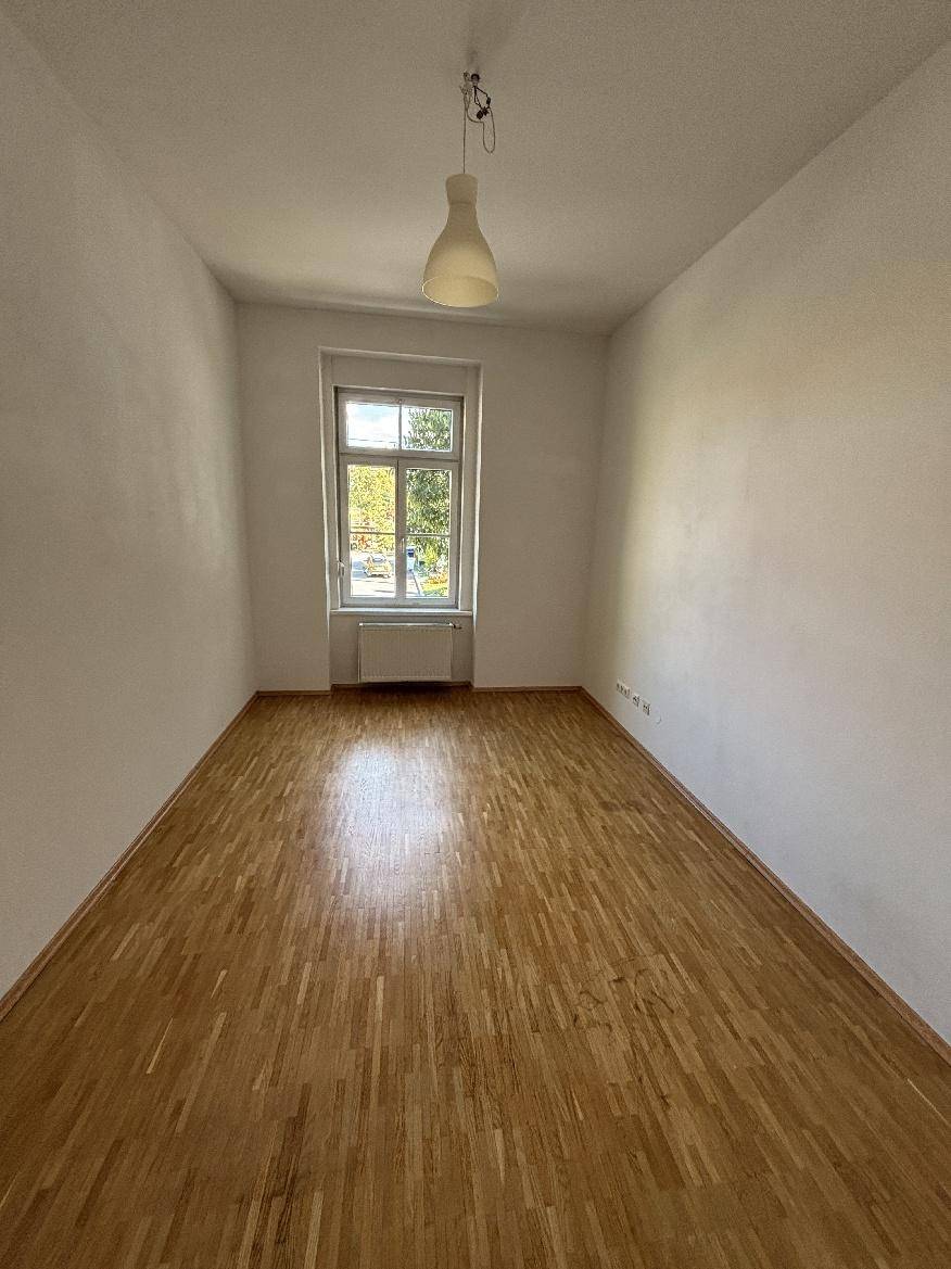 Leeres Zimmer mit Parkettboden, weiß gestrichenen Wänden und einem großen Fenster.