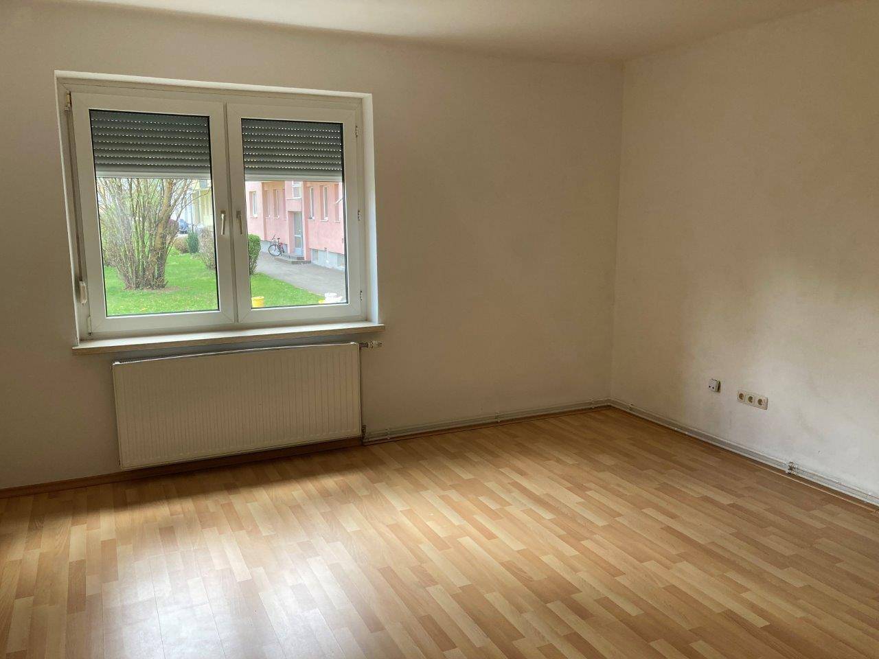 Geräumiges Zimmer mit Laminatboden, großem Fenster und Blick ins Grüne.