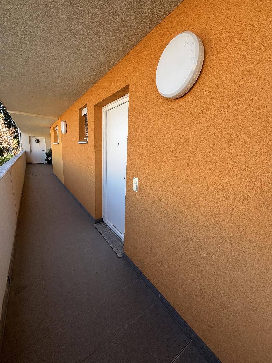 Außenflur mit orangefarbener Fassade und Zugang zu den Wohneinheiten.